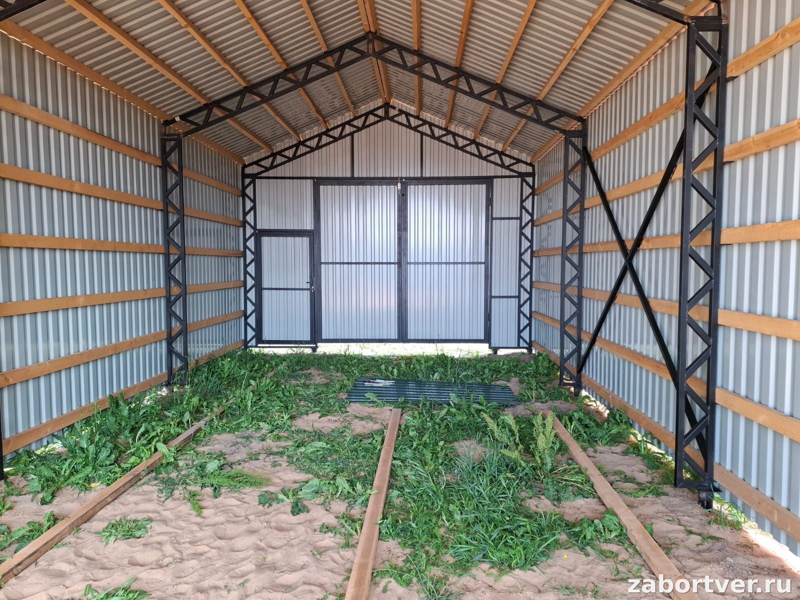 Внутренний вид каркасного гаража: металлические фермы, деревянная обрешетка, обшивка серым профнастилом и распашные ворота