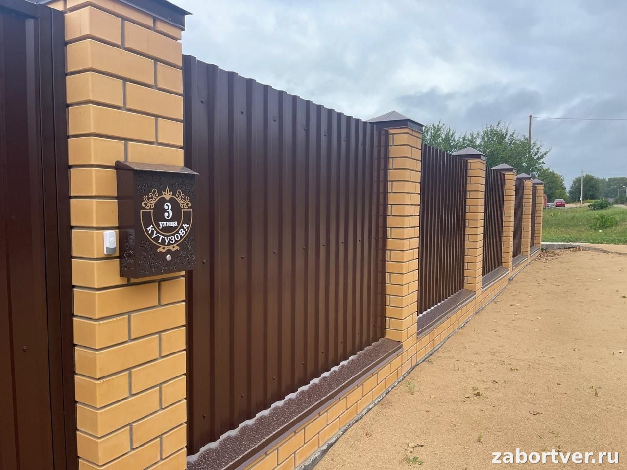 Забор из коричневого профнастила с желтыми кирпичными столбами и установленным почтовым ящиком, фото выполненного монтажа в Твери
