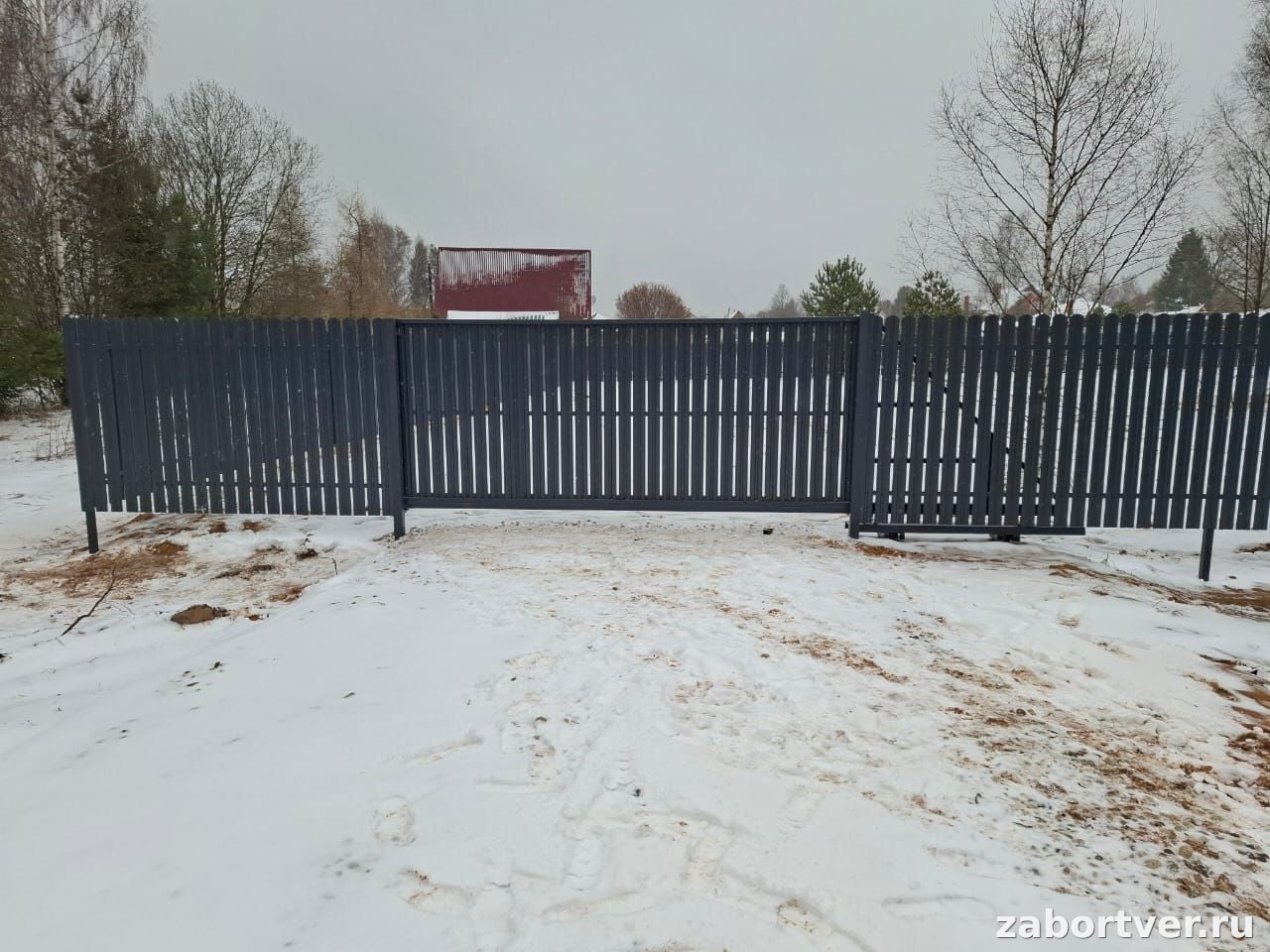 Темно-серый забор из металлического штакетника с закрытыми откатными воротами на фоне зимнего пейзажа, работа ЗаборТверь
