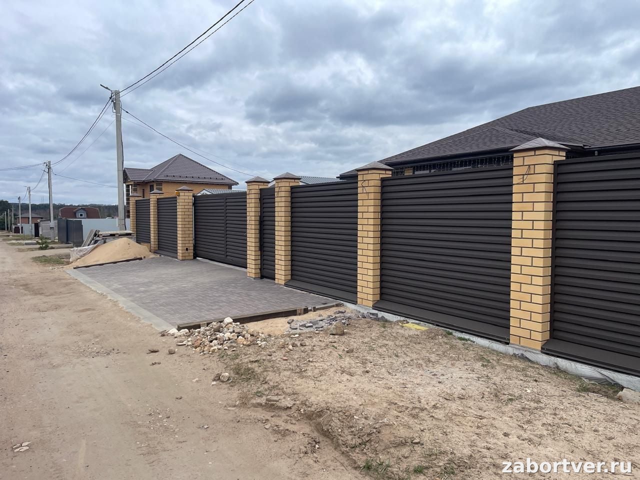 Глухой коричневый забор жалюзи с желтыми кирпичными столбами и откатными воротами на участке