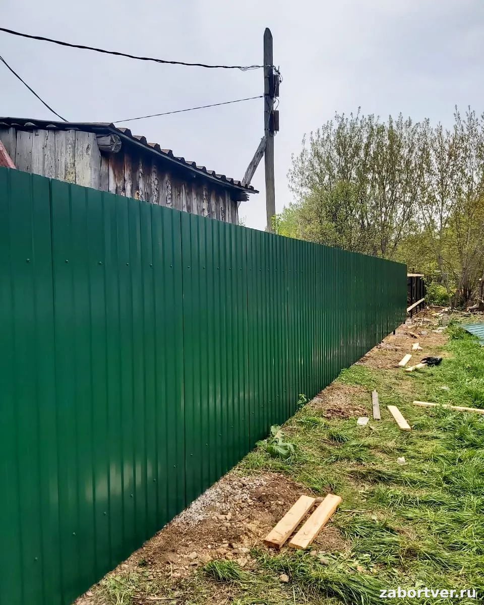 Длинный зеленый забор из профнастила, установленный на дачном участке, вид снаружи
