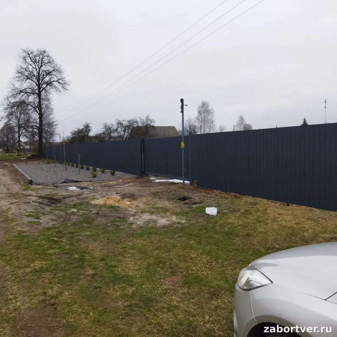 Высокий глухой забор из темно-серого профнастила с автоматическими откатными воротами на участке