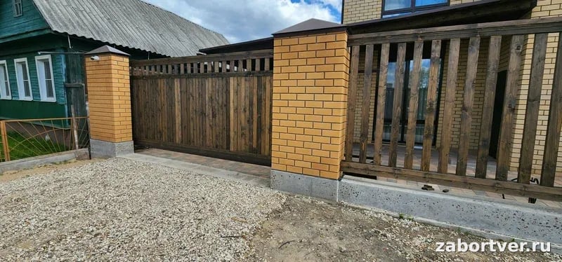 Откатные ворота из темного дерева и забор на столбах из желтого кирпича, строительство под ключ от ЗаборТверь