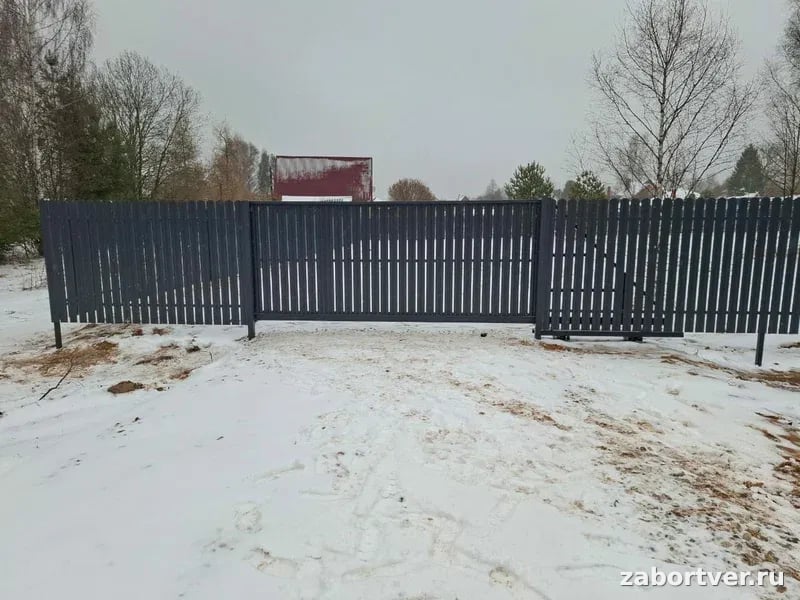 Темно-серый забор из металлического евроштакетника с закрытыми откатными воротами на заснеженном участке