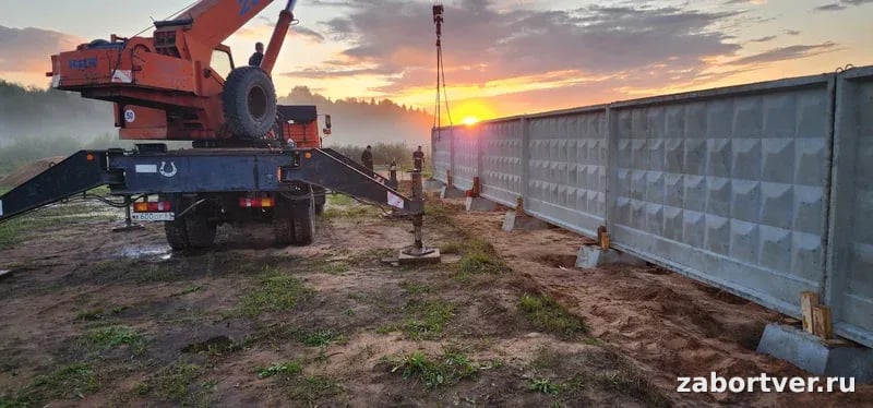 Установка железобетонного забора ПО-2 автокраном на закате, монтаж бетонных плит в фундаментные стаканы, спецтехника в работе