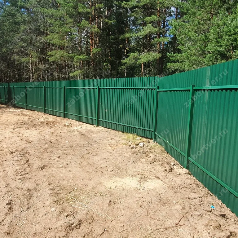 Классический забор из зеленого профнастила, установленный на металлический каркас из профильных труб. Надежное и долговечное ограждение участка, гармонично вписывающееся в лесной ландшафт.